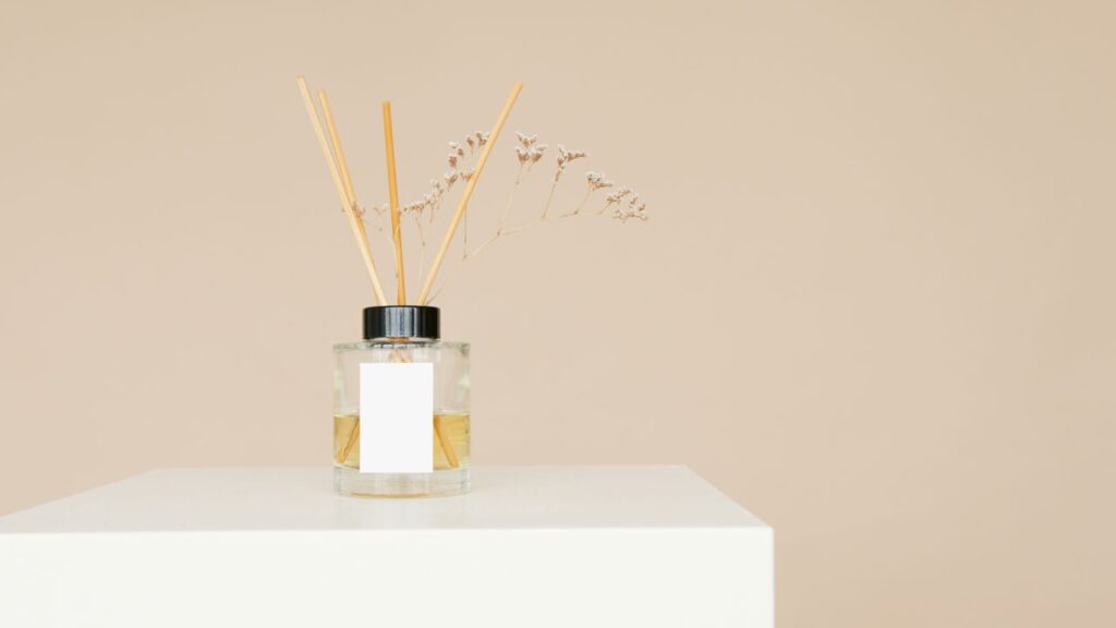 A minimalist reed diffuser with a mockup label on a white pedestal against a neutral background.